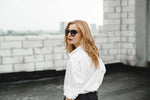 Stylish model in white shirt and sunglasses showcasing luxury streetwear vibes against a Barcelona skyline backdrop.