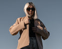a woman with white hair wearing a tan jacket and sunglasses