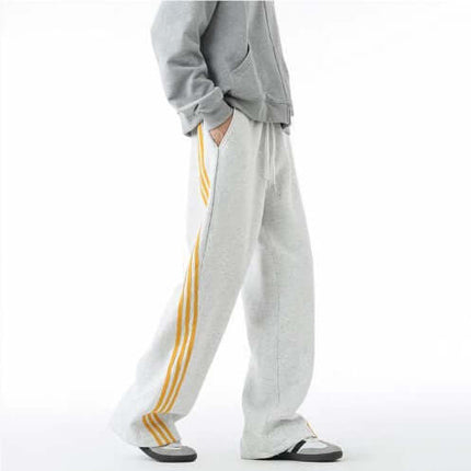 Heavyweight Three-Stripe Pants - Loose Fit in grey with yellow stripes being worn by a person.