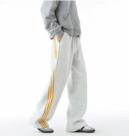 Heavyweight Three-Stripe Pants - Loose Fit in grey with yellow stripes being worn by a person.