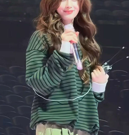 A person wearing a striped lapel polo shirt, smiling and holding a microphone, in a casual setting.