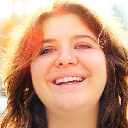 Radiant smile of a joyful young woman, epitomizing warmth and positivity against a sunlit backdrop.