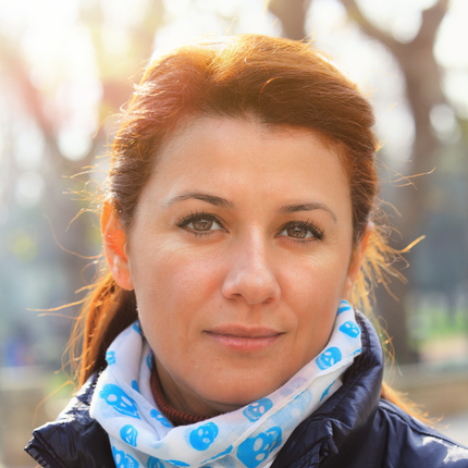 Portrait of a woman in a navy jacket, framed by natural light, showcasing a stylish blue skull-printed scarf.