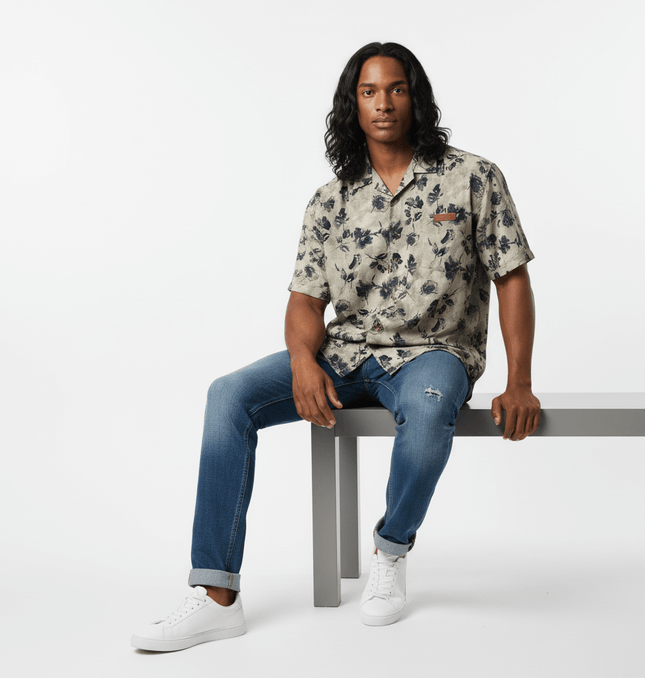 Floral Print Short Sleeve Shirt – Loose Fit worn by a model sitting on a bench, showcasing casual summer style.