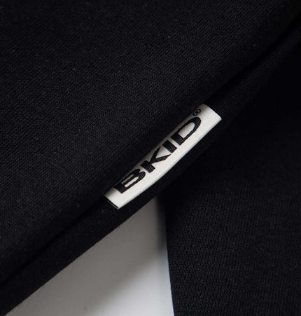 Close-up of the BKID tag on a black hoodie, showcasing brand detail.