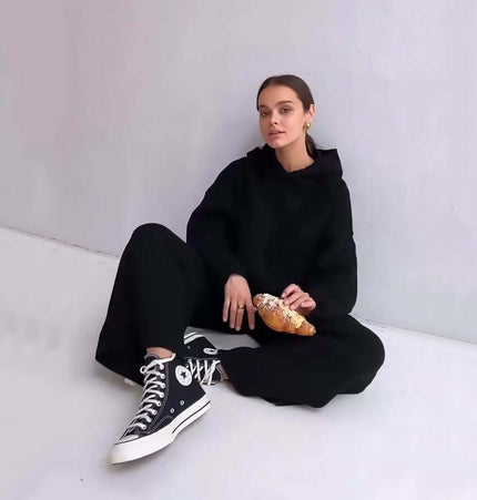 Cotton Blend Two-Piece Sports Set model sitting in casual black outfit with hoodie and sneakers holding a croissant.
