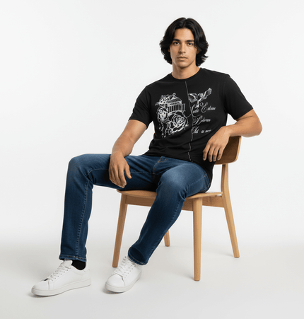 Drop Shoulder Printed TShirt – Loose Fit model in black letter print sitting on a chair wearing jeans and sneakers.