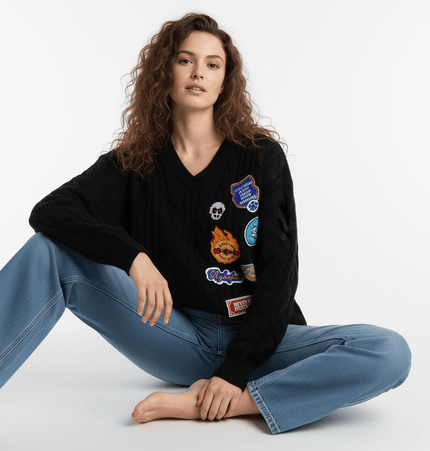 Embroidered Cable Knit VNeck Sweater worn by a model sitting, showcasing its unique patches and relaxed fit.