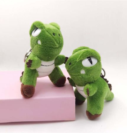 Green Dinosaur Plush Keychain featuring cute cartoon-style plush dinosaurs on a pink background.