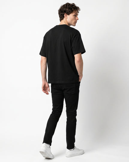 Full body rear view of model Jax wearing GROZAVU Black T-Shirt showcasing rear garment structure and back artwork