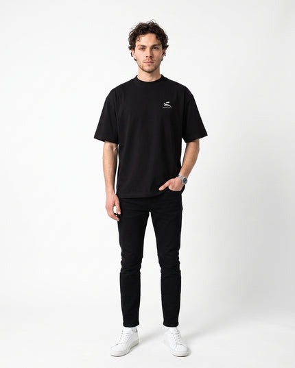 Straight-on front full-body view of model Jax wearing GROZAVU Black T-Shirt in seamless white studio