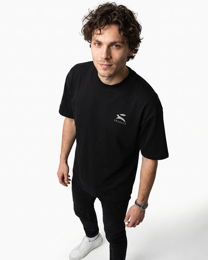 Dynamic 3/4 angled upper-body zoom of model Jax wearing GROZAVU Black T-Shirt highlighting garment drape, fit, and side profile