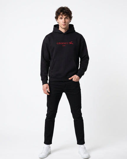 Straight-on front full-body view of model Jax wearing GROZAVU SS26 Black Hoodie in seamless white studio