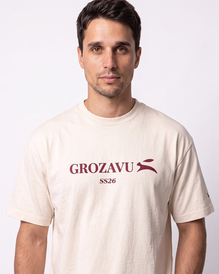 Dynamic close-up portrait of GROZAVU SS26 Cream T-Shirt highlighting crisp chest branding and luxury fabric texture