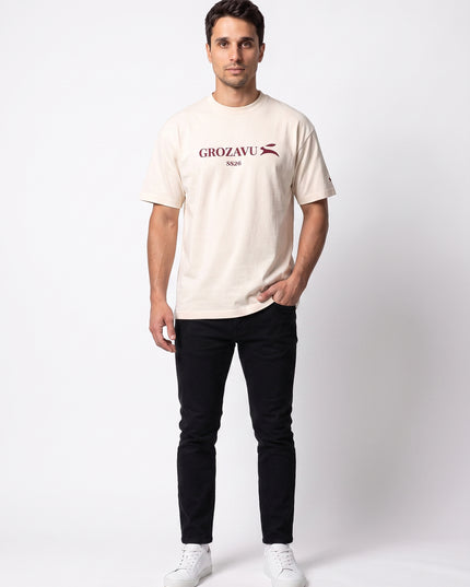 Straight-on frontal streetwear power stance of model Lucas wearing GROZAVU SS26 Cream T-Shirt in luxury studio setting