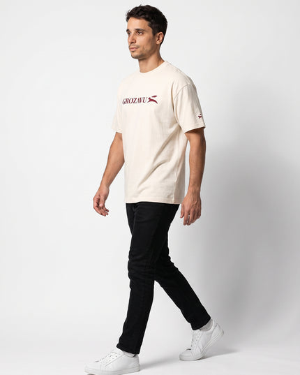 Dynamic 3/4 side profile hero stride of GROZAVU SS26 Cream T-Shirt worn by model Lucas in luxury studio lighting