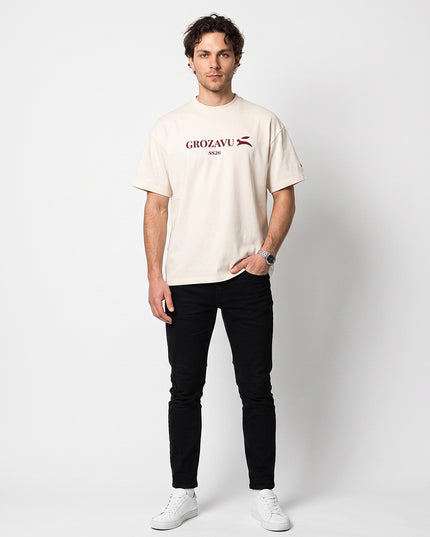 Straight-on front full-body view of model Jax wearing GROZAVU SS26 Off-White T-Shirt in seamless white studio