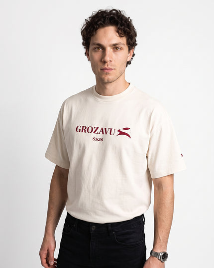 Dynamic 3/4 angled upper-body zoom of model Jax wearing GROZAVU SS26 Off-White T-Shirt highlighting garment drape, fit, and side profile