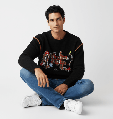 Knit Sweater with Letter Applique worn by a man sitting cross-legged, showcasing its artistic design and casual style.