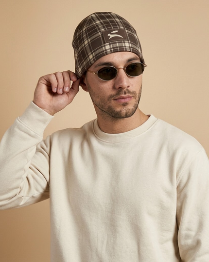 Model adjusting the Heritage Tartan Beanie in Cocoa, waist-up studio shot