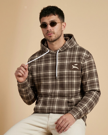 Close-up of the Grozavu hare patch on the Heritage Tartan Hoodie in Cocoa, worn by the model