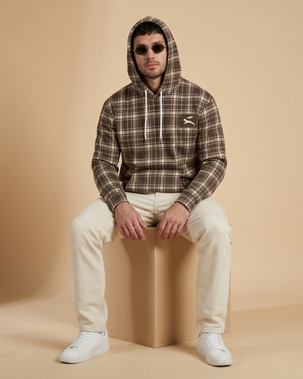 Model seated in the studio wearing the Heritage Tartan Hoodie in Cocoa with the hood up