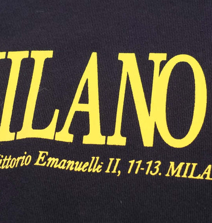Close-up of yellow text on a dark fabric featuring "MILANO" and an address, highlighting urban street style.