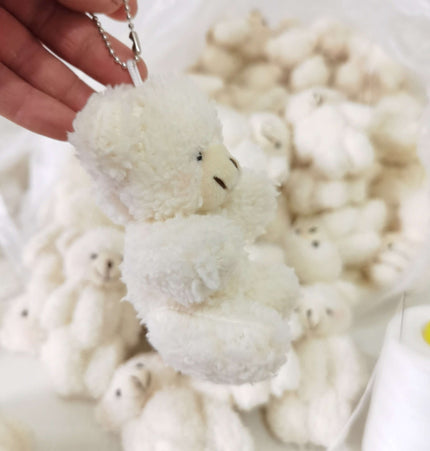 A hand holding the Shy Blush Bear Plush Keychain among a pile of plush bears.