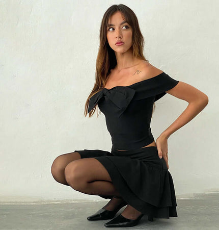 Slim Fit One-Shoulder Bow Top worn by a woman posing elegantly in a black skirt and heels.
