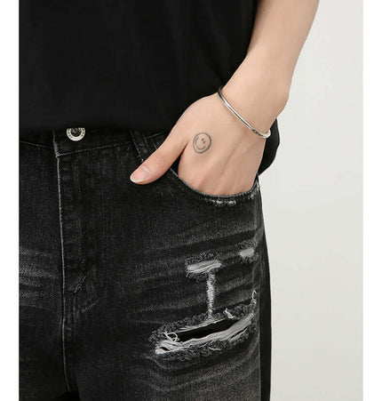 Washed Distressed Straight Jeans – Loose Fit shown with hand in pocket, featuring a vintage black wash and distressed detailing.