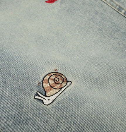 A close-up of the Grozavu Washed Straight Cropped Jeans showcasing a cute snail embroidery detail on light blue denim.